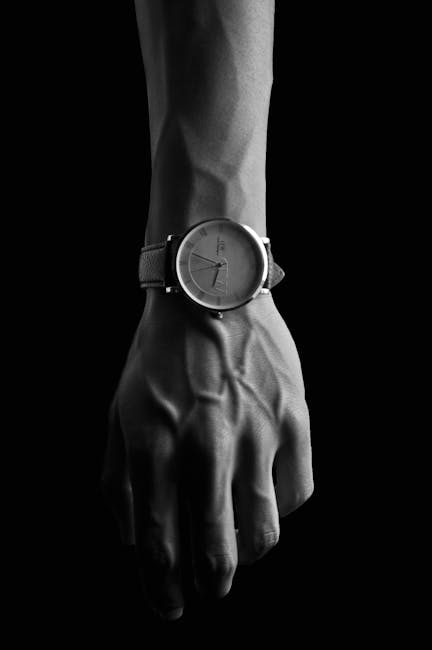 Black and white image showcasing a wristwatch on a man's hand, emphasizing veins and minimalism.