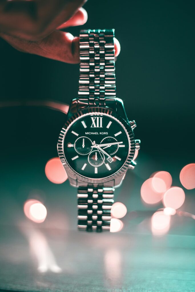 Silver Michael Kors wristwatch with Roman numerals and elegant design, highlighted by bokeh lights.